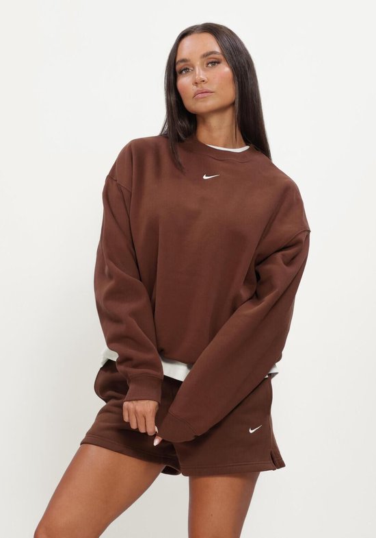 Een vrouw in een bruine Nike sweater en bijpassende shorts. De sweater heeft een kleine witte Nike 'swoosh'.