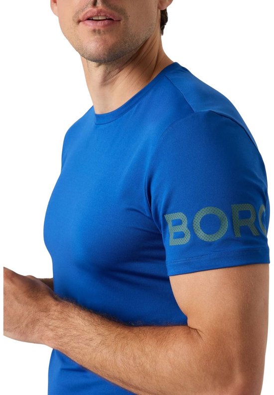 Close-up van een man in een kobaltblauw sportshirt, logo 'BORG' met stipjes op de mouw.