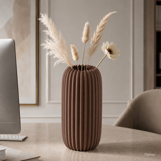 Chocoladebruine, geribbelde vaas met pampagras en een witte bloem, op een bureau.