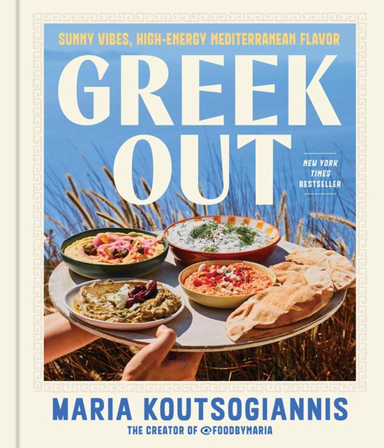 Kookboek 'Greek Out' van Maria Koutsogiannis met een schaal vol Griekse dips en pitabrood in een zonnig landschap.