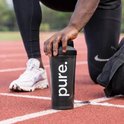 Zwarte 'pure.' shakebeker vastgehouden door atleet op een hardloopbaan.