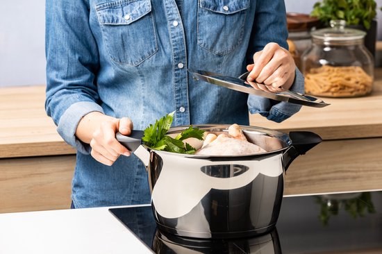 Vrouw in spijkerblouse met zwarte handvatten, met roestvrijstalen kookpot met kip en groenten.
