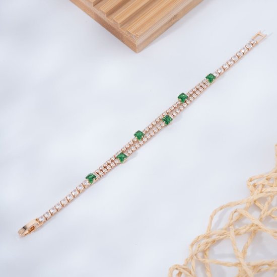 Goudkleurige tennisarmband met twee rijen witte zirkonia en verspreide groene vierkante stenen op een witte achtergrond.