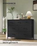Zwart dressoir met zeven stoffen lades, geplaatst in een woonkamer naast een trap.