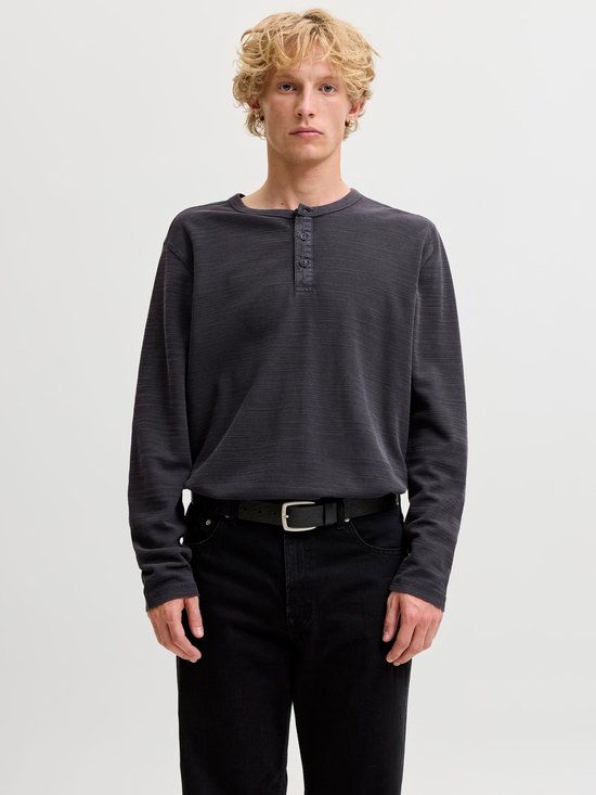 Model draagt een antracietgrijze henley-top met lange mouwen, knoopsluiting en structuurpatroon met zwarte jeans.