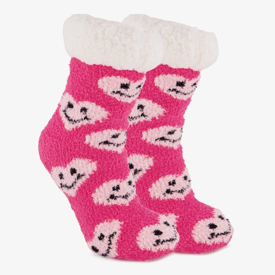 Roze, pluizige huissokken met een wit, wollig boord en een patroon van roze hartjes met lachende gezichtjes.