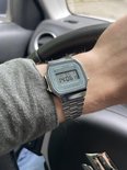 Casio horloge met zilverkleurige metalen band en groen wijzerplaat met digitale tijdsaanduiding. "ILLUMINATOR", "WATER RESIST"