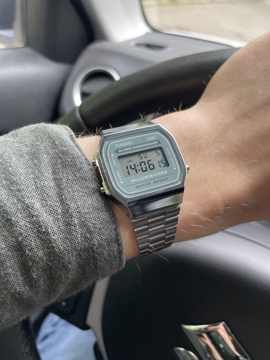 Casio horloge met zilverkleurige metalen band en groen wijzerplaat met digitale tijdsaanduiding. "ILLUMINATOR", "WATER RESIST"