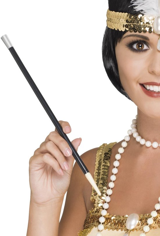 Een vrouw met een parelketting en hoofdband houdt een zwarte sigarettenhouder vast. Goudkleurige pailletten op de jurk.