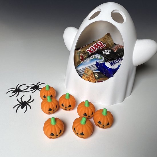 Witte spookvormige snoepkom gevuld met Twix, Milky Way en andere chocolaatjes, met kleine oranje pompoenen op tafel.