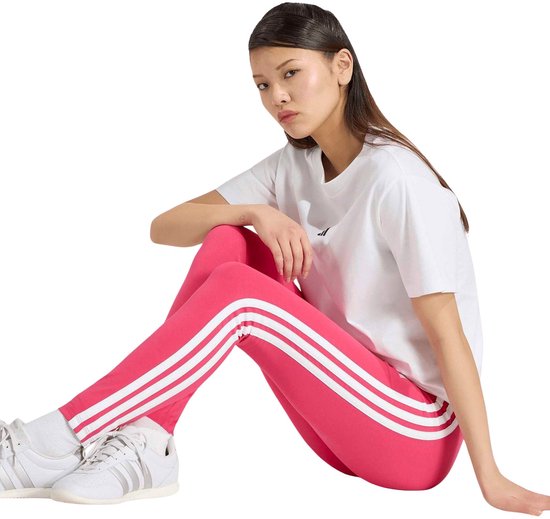 Model zittend in roze adidas legging met witte zijstrepen, wit t-shirt en witte sneakers.