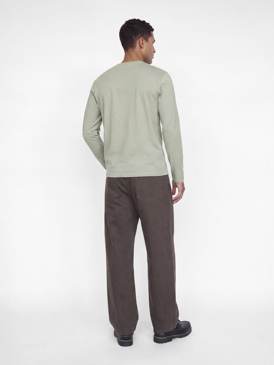 Achteraanzicht van het model in een lichtgrijs T-shirt met lange mouwen en een donkerbruine broek.