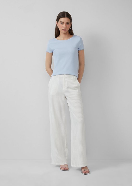 Model van voren gezien, draagt een lichtblauw t-shirt en een witte broek met wijde pijpen en krijtstrepen.