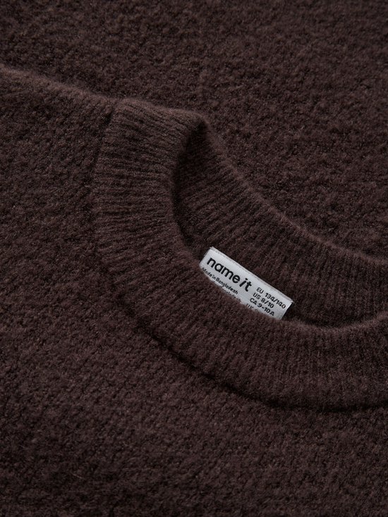 Close-up van de textuur van een bruine gebreide jurk met NAME IT label in de nek.