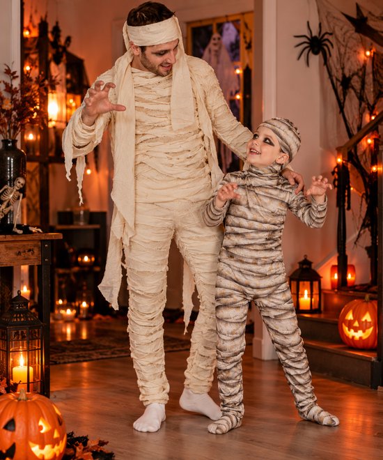 Vader en kind in mummiekostuum met wit verband, inclusief bijpassende hoofdkap in een griezelige Halloween-omgeving.