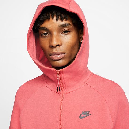 Model met koraalroze Nike Tech Fleece-hoodie met capuchon op, Nike-logo op de borst.