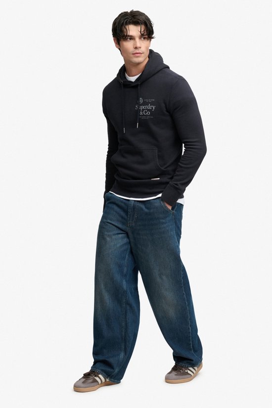 Model draagt donkerblauwe hoodie, wijde jeans en sneakers.