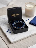 Donkerblauwe, facetgeslepen glazen kralen met goudkleurige accenten, gevlochten tot een armband in een open Luxamore sieradendoosje.