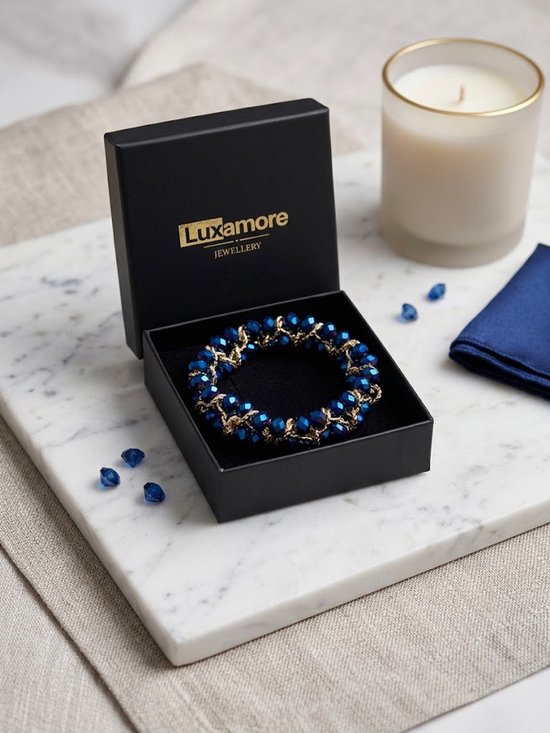 Donkerblauwe, facetgeslepen glazen kralen met goudkleurige accenten, gevlochten tot een armband in een open Luxamore sieradendoosje.