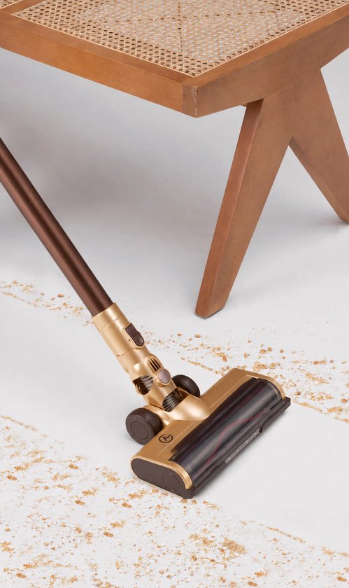 Gouden en bruine steelstofzuigerkop met donker houtdetail, zuigt kruimels op bij een houten stoelpoot.
