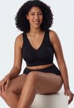 Vrouw met krullend haar in zwarte bustier en bijpassende slip, zittend.