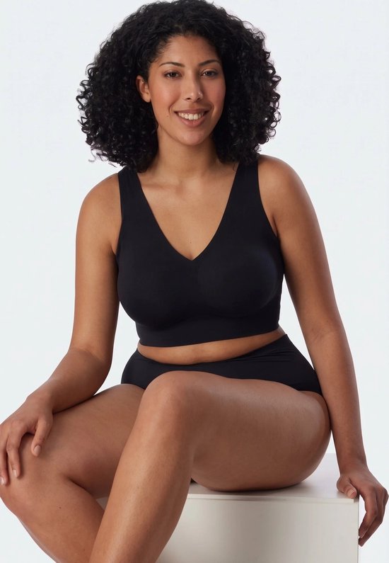 Vrouw met krullend haar in zwarte bustier en bijpassende slip, zittend.