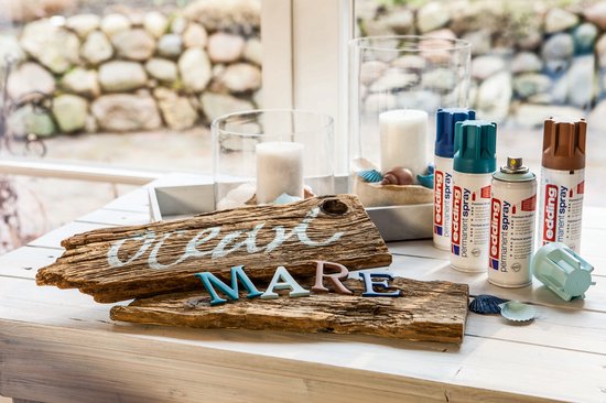 Houten bord met tekst 'Ocean Mare', letters, edding spuitbussen en schelpen op een houten tafel.