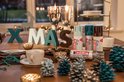 Kerstdecoratie met 'XMAS' letters, drie edding spuitbussen, kaarsen, dennenappels en tafelservies.