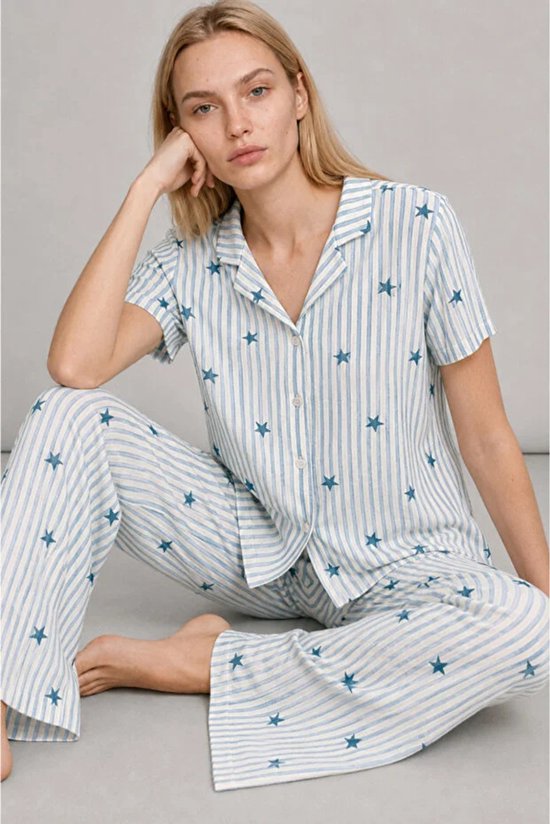 Model in een lichtblauwe, wit gestreepte pyjamaset met sterren, zittend op de grond.