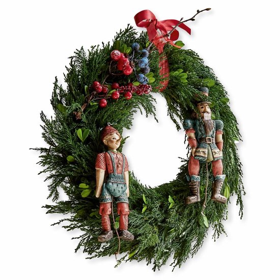 Groene kerstkrans met rode bessen, blauwe vruchten, rode strik en twee houten notenkrakerfiguren.