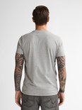 Achteraanzicht van het grijze t-shirt gedragen door een getatoeëerd model, in combinatie met een donkergrijze jeans.