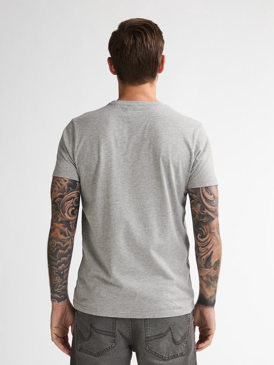 Achteraanzicht van het grijze t-shirt gedragen door een getatoeëerd model, in combinatie met een donkergrijze jeans.