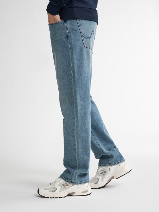 Een man draagt een losse, lichtblauwe spijkerbroek van Petrol Industries met een casual pasvorm. De broek heeft een lichte wassing en klassieke jeanszakken.