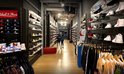 Winkelinterieur van een sportkledingwinkel met rekken vol sneakers, baseballpetten en kleding.