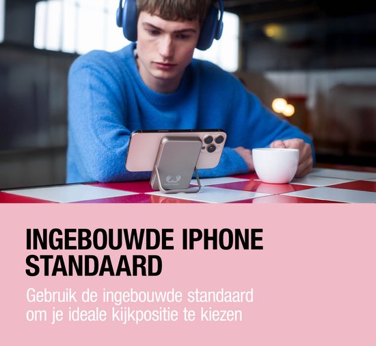 Grijze powerbank met ingebouwde standaard, ondersteunt een iPhone terwijl een man met koptelefoon kijkt.