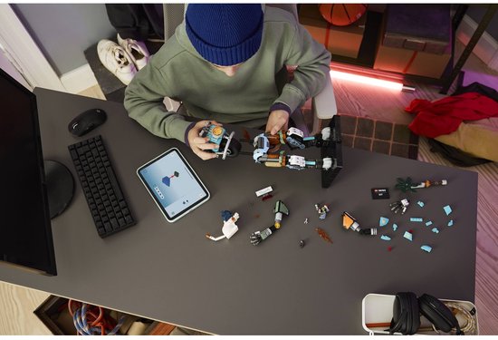 Garçon avec bonnet bleu construisant le kit LEGO Fortnite à un bureau, avec tablette et pièces détachées.