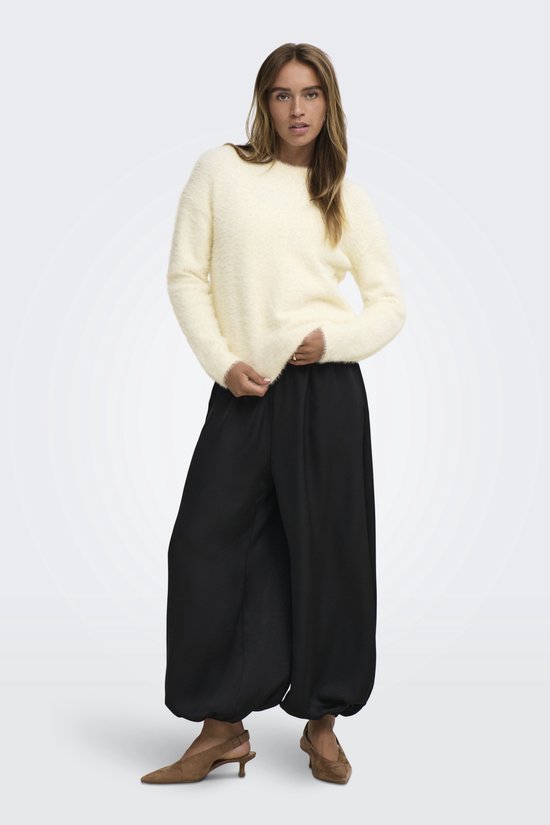 Model in crèmekleurige, pluizige trui en zwarte broek met wijde pijpen.