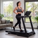 Vrouw met een VirtuFit hartslagmeter om haar borst, gekleed in sportkleding, traint op een loopband in een woonkamer.