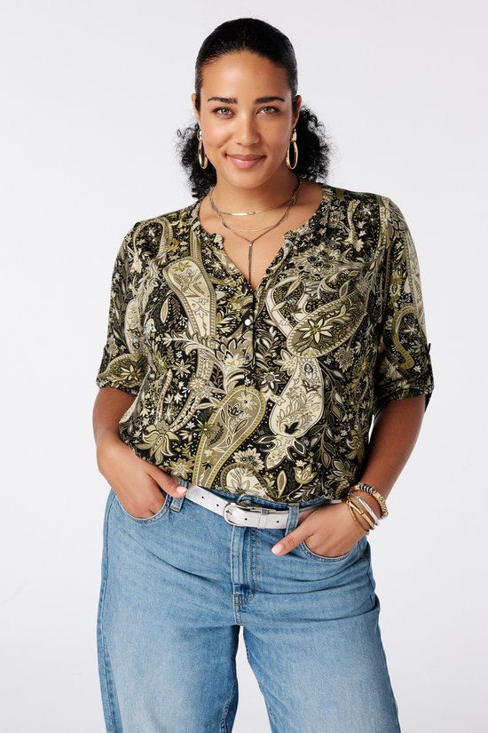 Model draagt een zwart shirt met paisleyprint in groen en beige en een witte riem, gecombineerd met een jeans.