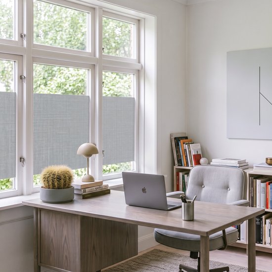 Kantoor aan huis met bureau, stoel en laptop bij een raam met grijze vouwgordijnen.