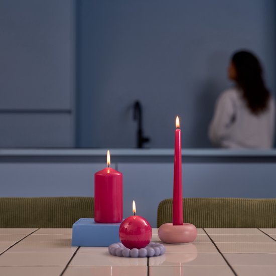 Twee fuchsia roze kaarsen, een stomp en een bol, op een tafel.