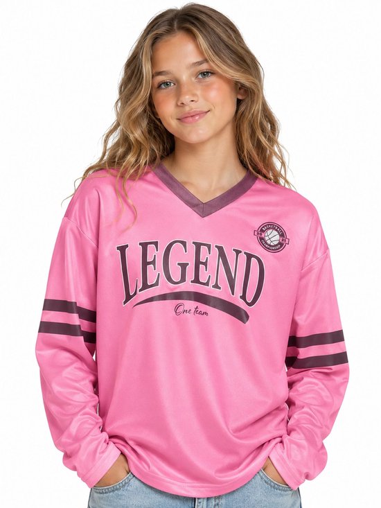 Een jong meisje draagt een roze longsleeve shirt met de tekst 'LEGEND' en 'One team'. Het shirt heeft een V-hals en donkere strepen op de mouwen.