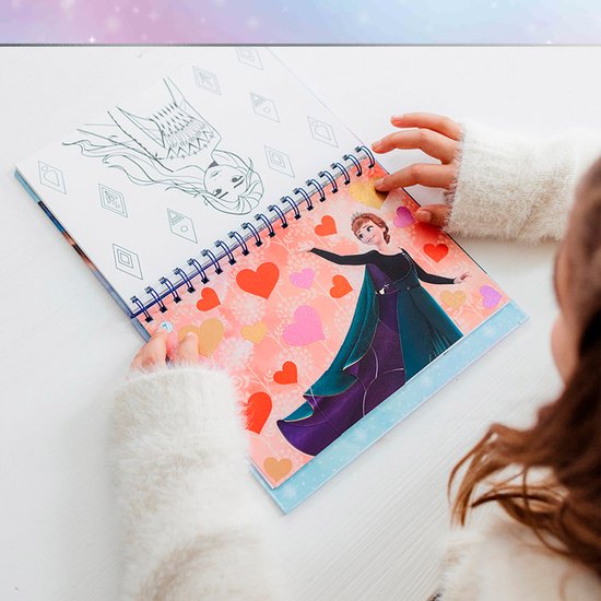 Enfant en gilet blanc collant des cœurs dans un livre d'autocollants La Reine des Neiges avec un coloriage d'Elsa.