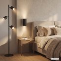 Zwarte Briloner vloerlamp met drie verstelbare geribbelde spots naast een bed in een modern interieur.