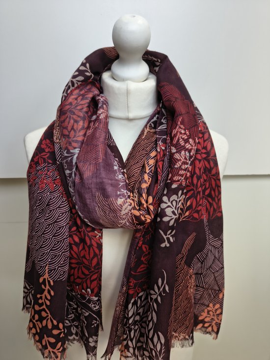Bordeauxrode sjaal met een print van bladeren en golvende lijnen in rood, oranje en crème, gedrapeerd over een paspop.