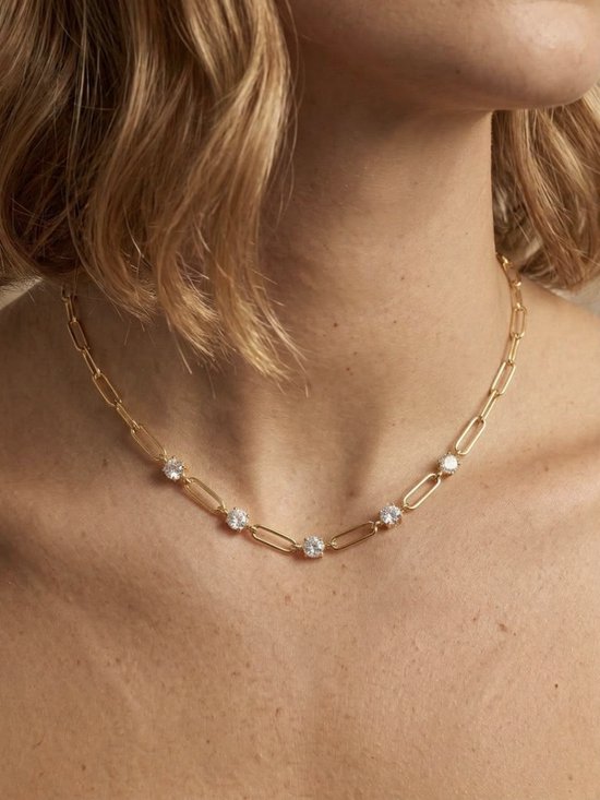 Gouden paperclip-ketting met vijf zirkonia-stenen gedragen om de nek.