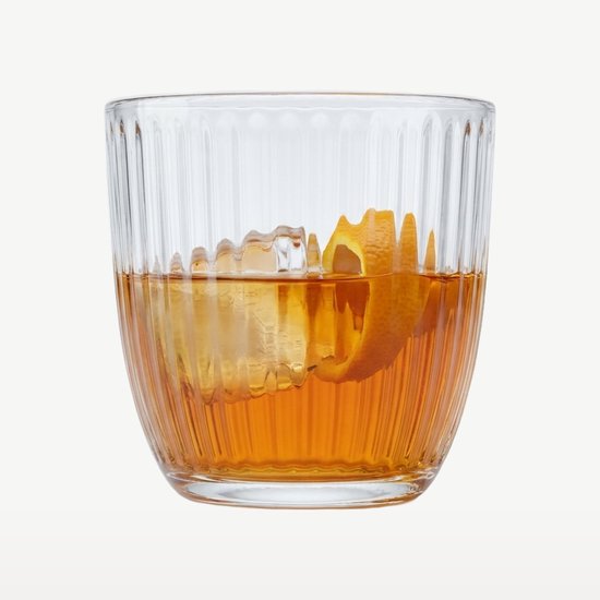 Verre à côtes verticales, rempli d'une boisson, de glaçons et d'un zeste d'orange.
