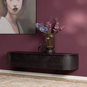 Zwart houten wandmeubel tegen een donkerrode muur, aangekleed met een vaas met bloemen en een decoratief beeldje.