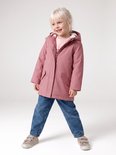 Meisje met blond haar, lachend, draagt een roze regenjas met teddy voering en spijkerbroek.
