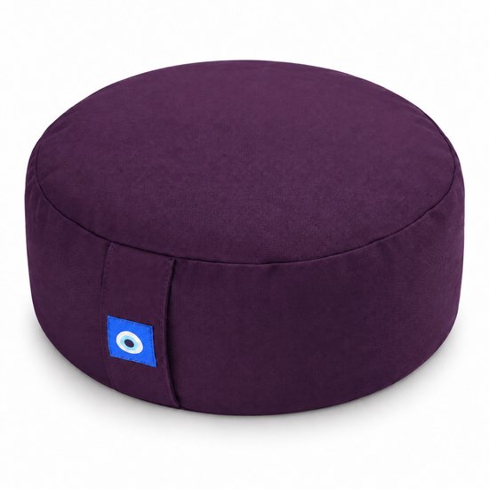 Rond, paars meditatiekussen met een opvallend blauw 'evil eye' label aan de zijkant.